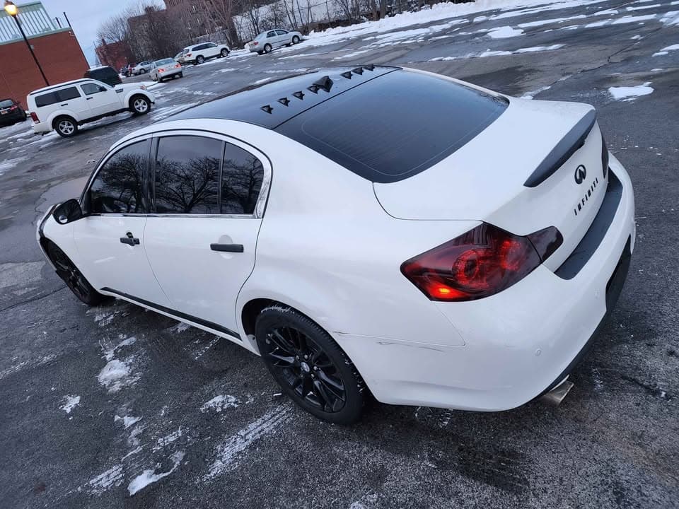 White Infiniti sedan with blacked-out roof and wheels on the lot in winter